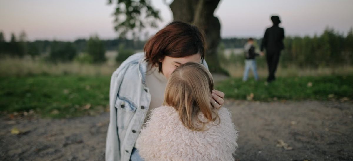 A tender moment between mother and daughter outdoors in a grassy field at twilight.