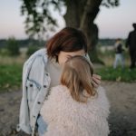 A tender moment between mother and daughter outdoors in a grassy field at twilight.